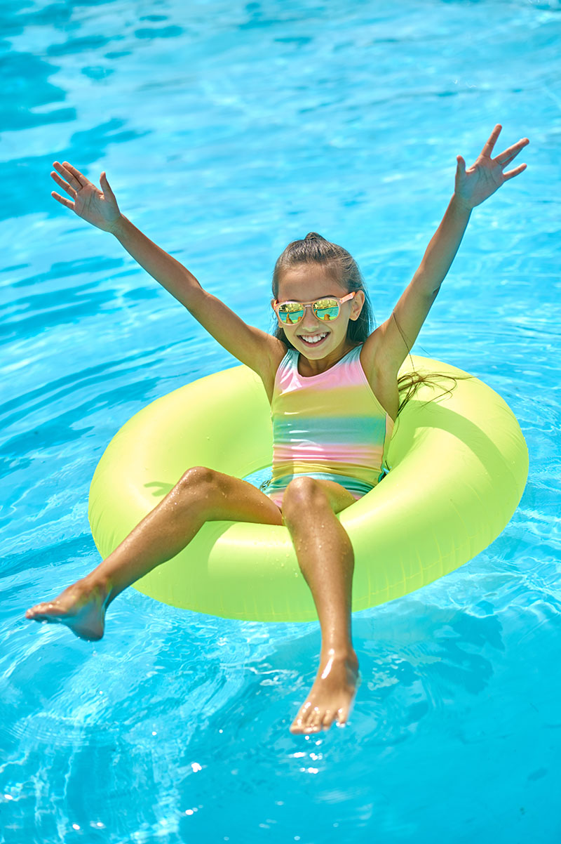 Delight. Top view of girl in sunglasses with raised hands sitting on inflatable ring on water smiling at camera